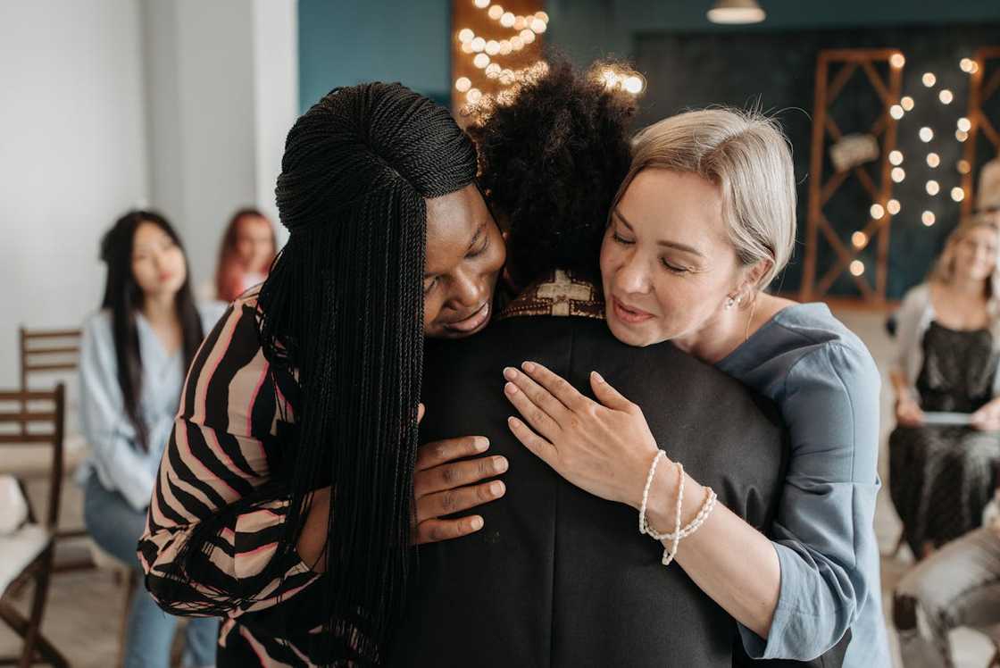 Two women hug another woman inside a church hall.