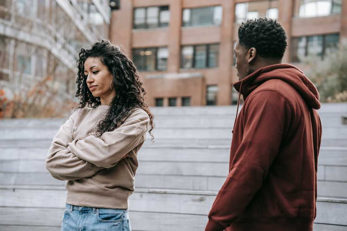 A woman with folded arms faces a man during an outdoor argument. A woman with folded arms faces a man during an outdoor argument.