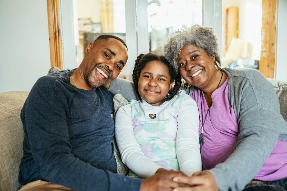 Three people sit close together on a couch, smiling warmly at the camera.