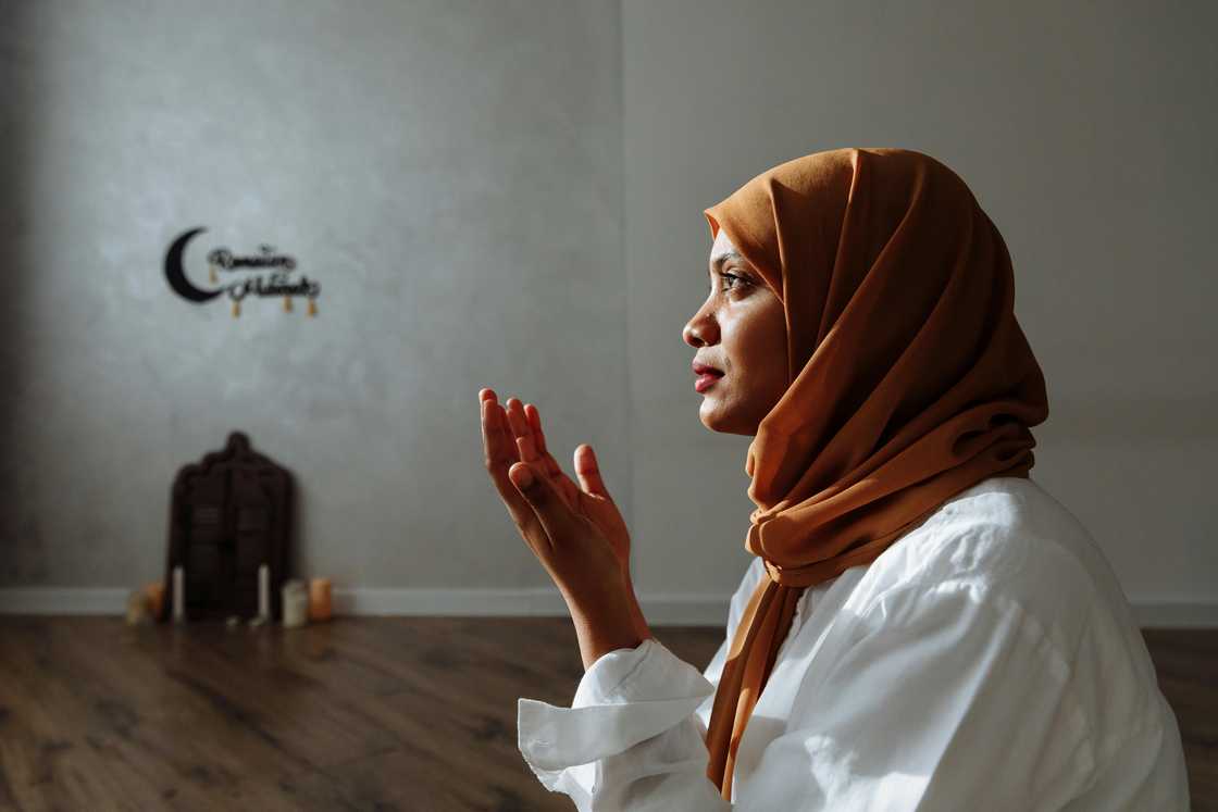 A woman in a white top and brown hijab is saying her Eid prayers