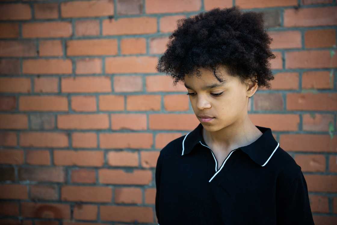 A teenage boy with an afro standing in front of a brick wall