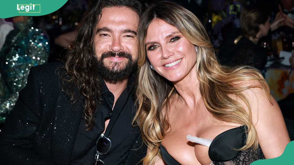 A man in a black sequined jacket with sunglasses stands close to a woman in a black lace and satin bustier dress. A man in a black sequined jacket with sunglasses stands close to a woman in a black lace and satin bustier dress.