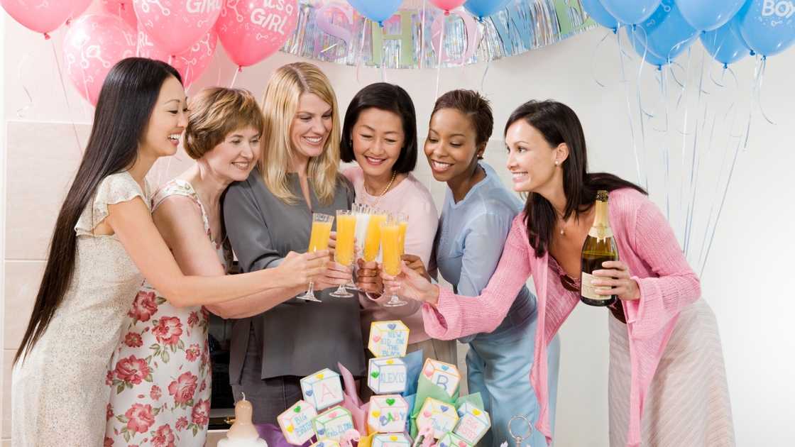 Women pose for a photo as they toast during a baby shower. Women pose for a photo as they toast during a baby shower.