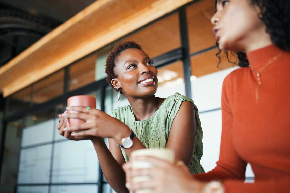 Two women in an office sharing a lively conversation over coffee