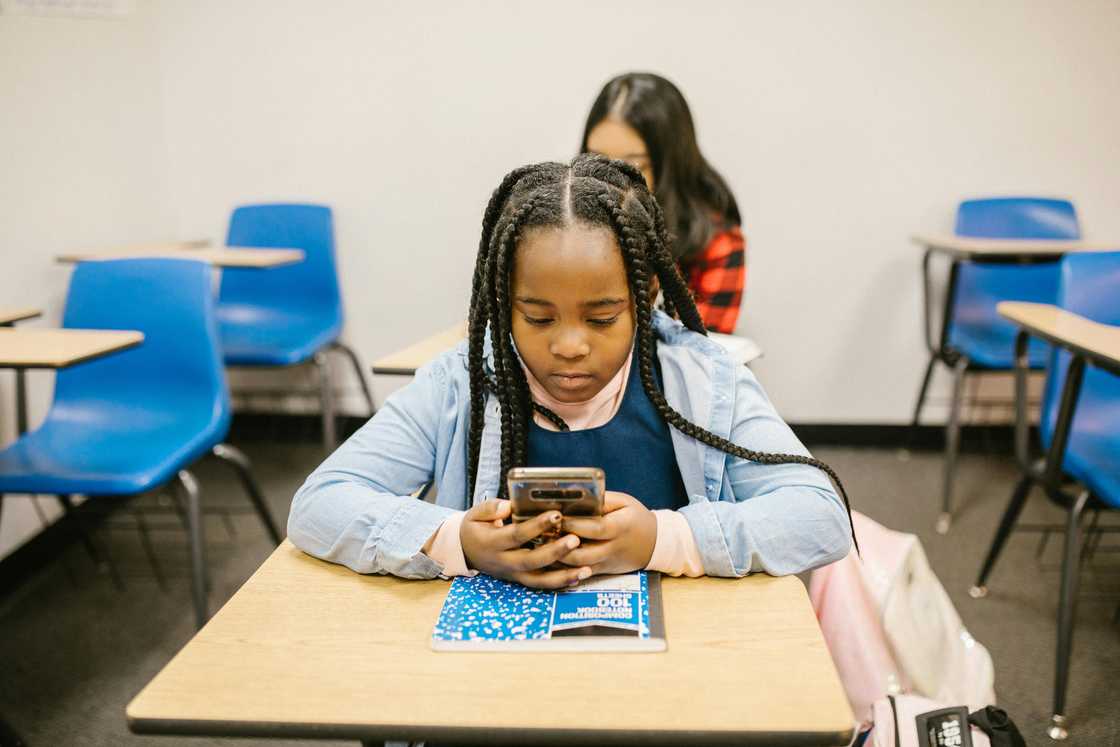 A girl sitting on her desk while using her smartphone