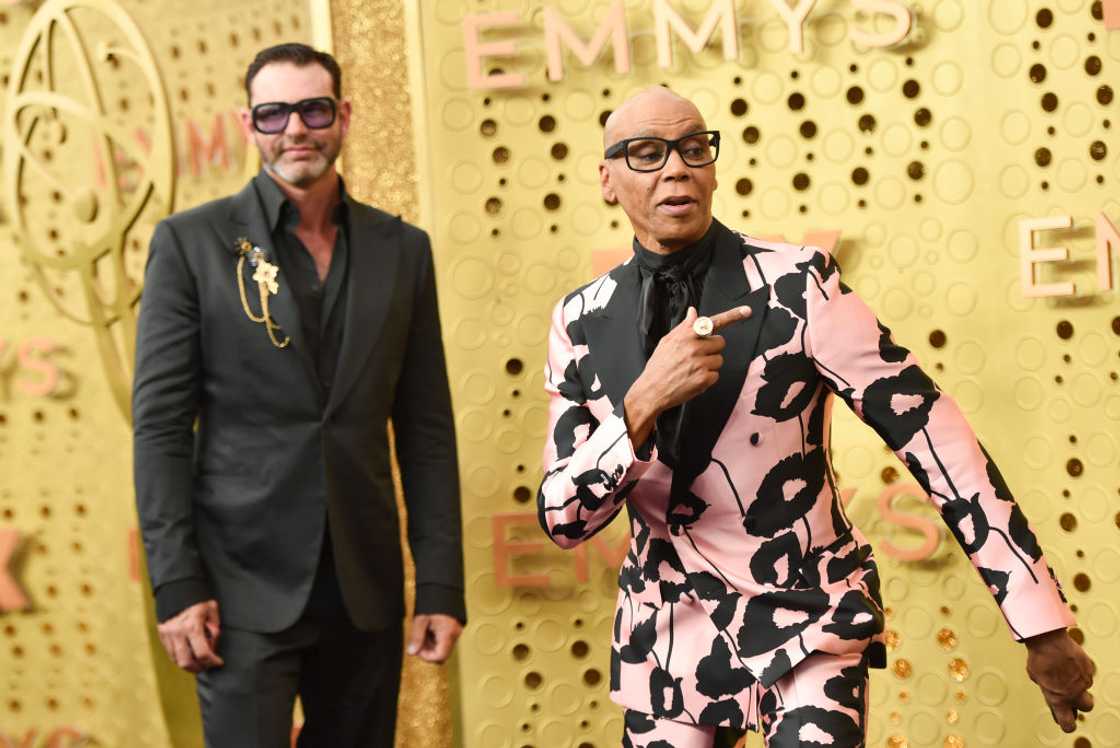 RuPaul in clear-framed glasses and a pink and black patterned suit beside his husband, Georges LeBar, in a black suit, at the Emmys RuPaul in clear-framed glasses and a pink and black patterned suit beside his husband, Georges LeBar, in a black suit, at the Emmys
