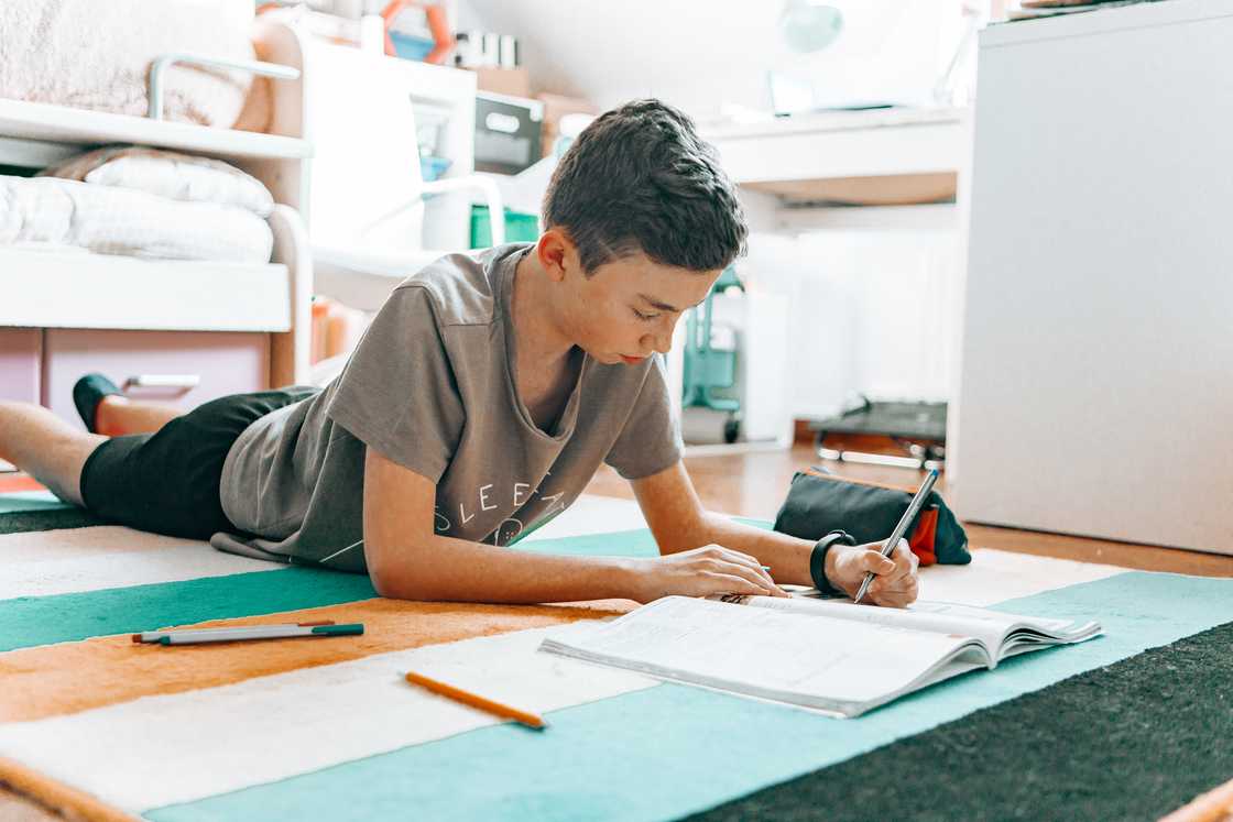 A boy drawing while lying on the floor