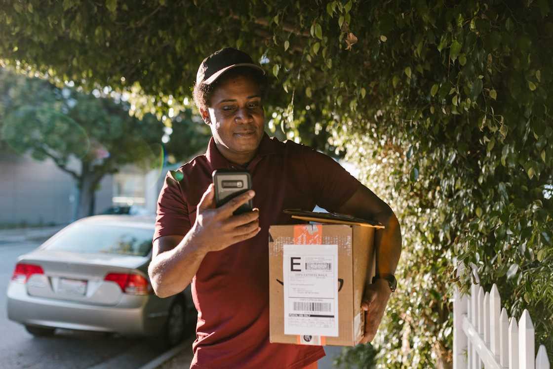 Courier holding a parcel and checking delivery details on phone.