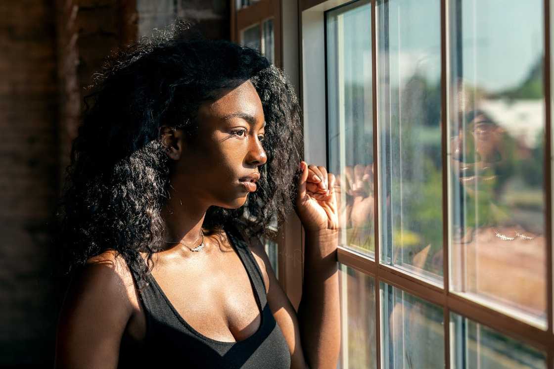 A woman reflects quietly near a window with soft daylight.