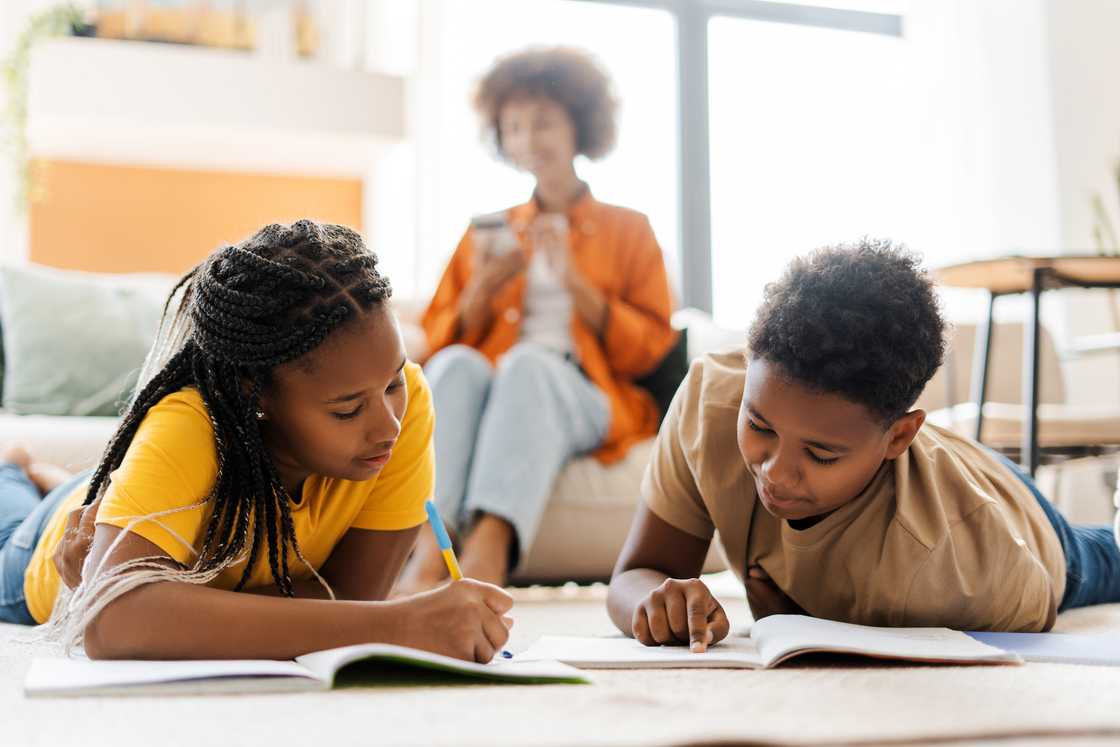 Children sketching ideas with their mother in the background.