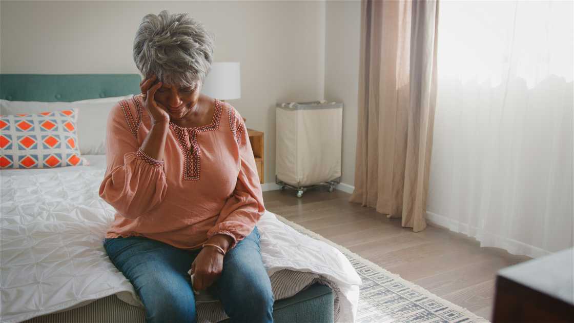 An elderly person sitting on bed holding her head. An elderly person sitting on bed holding her head.