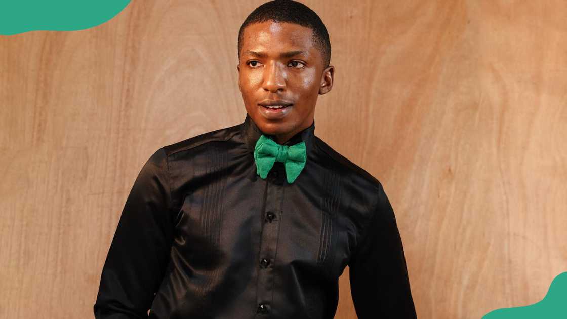 A young man wearing a black tuxedo shirt and a gree bow tie.