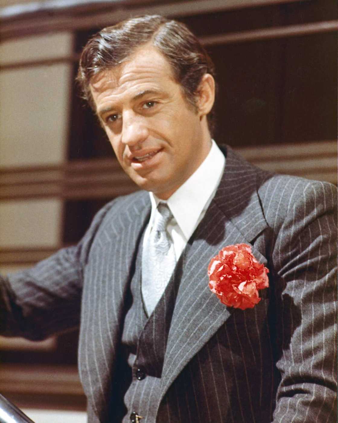 Jean-Paul Belmondo, acteur français, jurant un costume à fines rayures bleu foncé, avec un gilet assorti, une chemise blanche et une cravate gris clair, avec une fleur rouge au revers, vers 1960. (Photo de Silver Screen Collection)