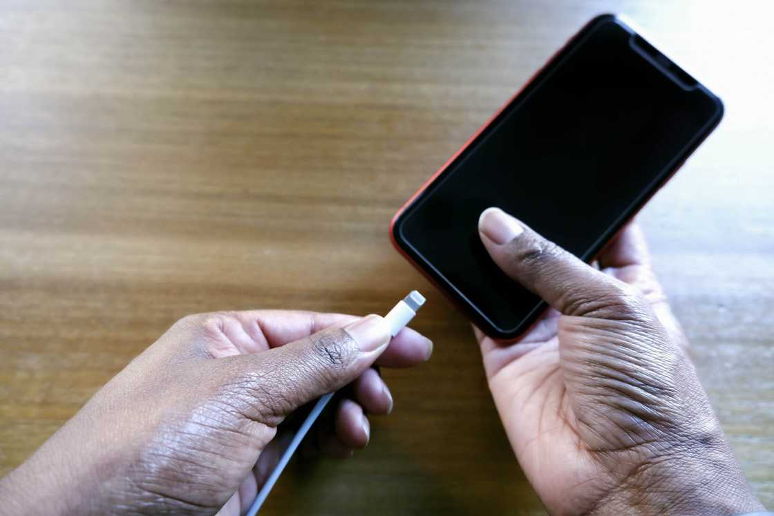 Close-up of a woman's hands holding a smart phone and charging cord.