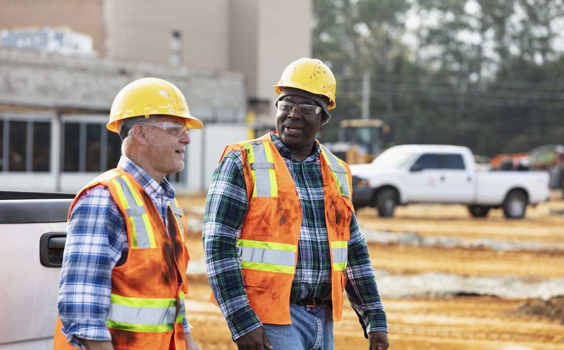 Two multiracial workers walking side by side at a construction site, conversing