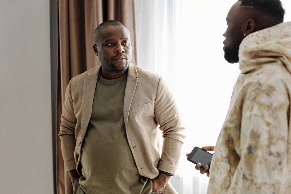 Two men talk in a modest living room.