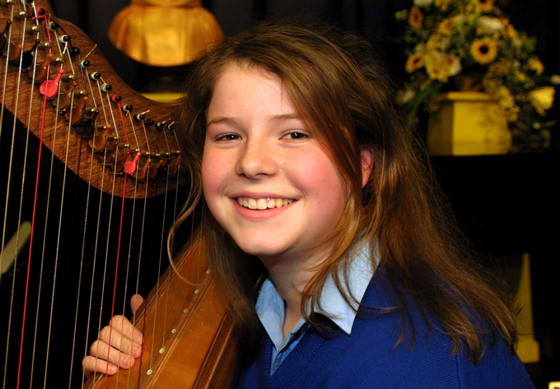 Jessie Buckley smiling while holding a wooden Celtic harp