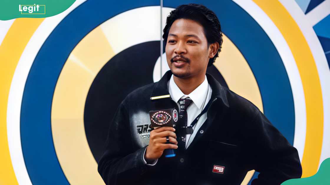 Aikou speaks before a blue and gold circular backdrop