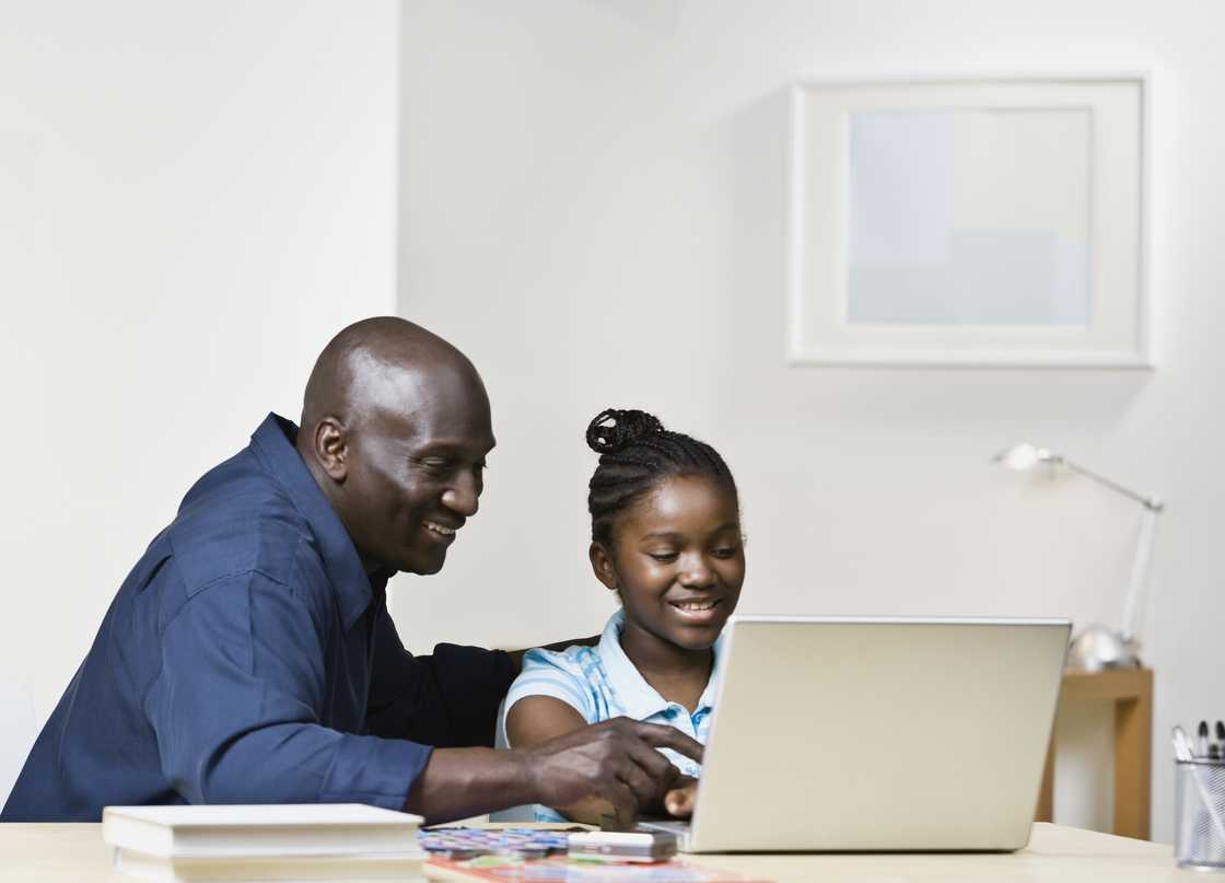 A parent watches as his daughter uses a laptop