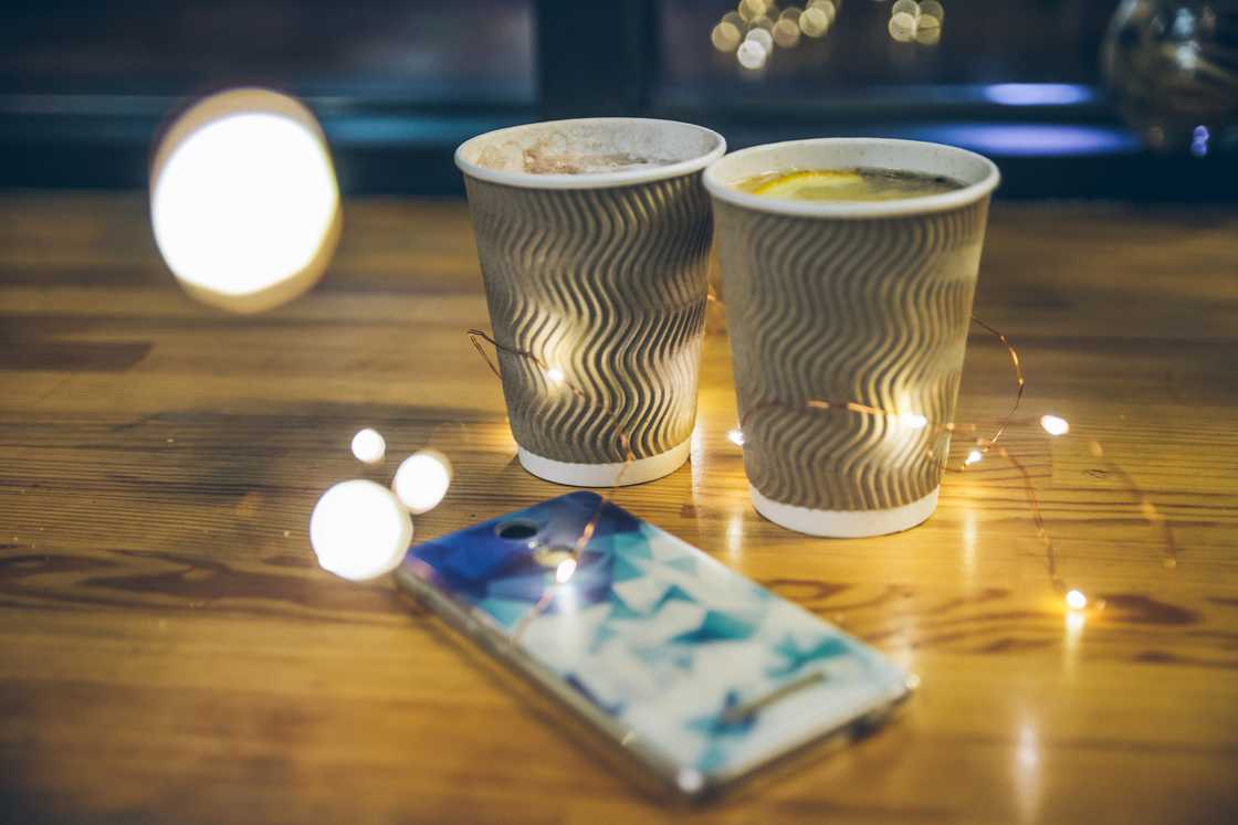 Two paper cups with hot drinks on a table, surrounded by fairy lights. Two paper cups with hot drinks on a table, surrounded by fairy lights.