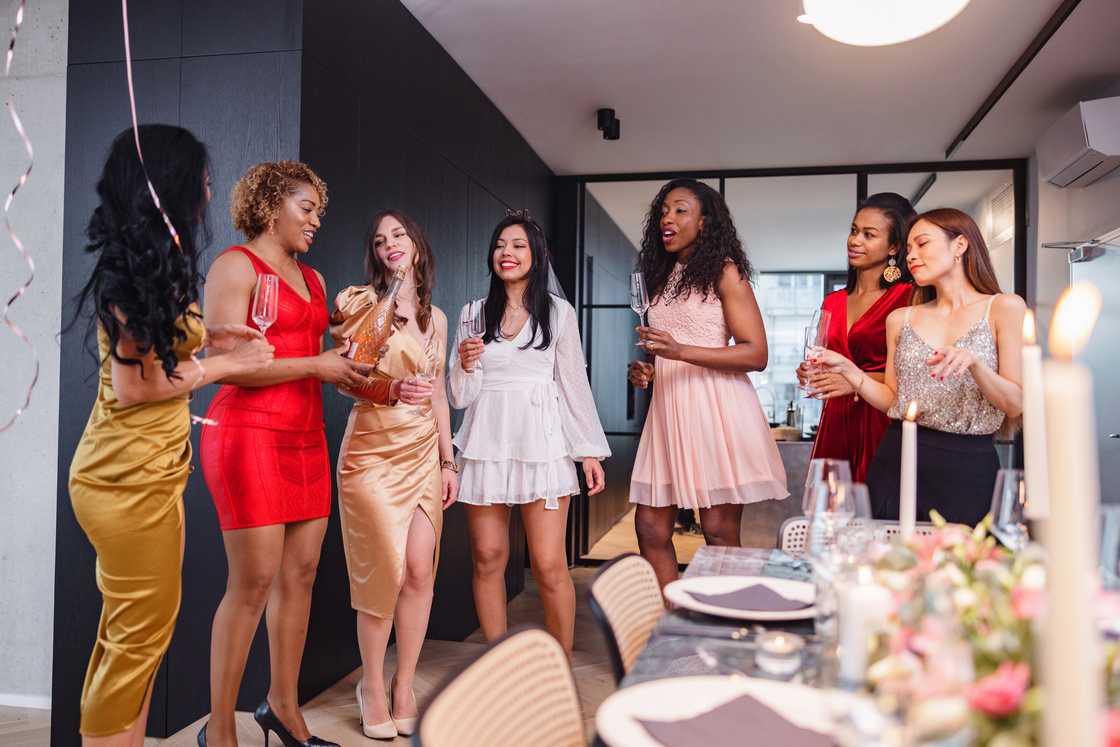 A group of best friends opening a bottle of champagne during a bachelorette party in a modern apartment