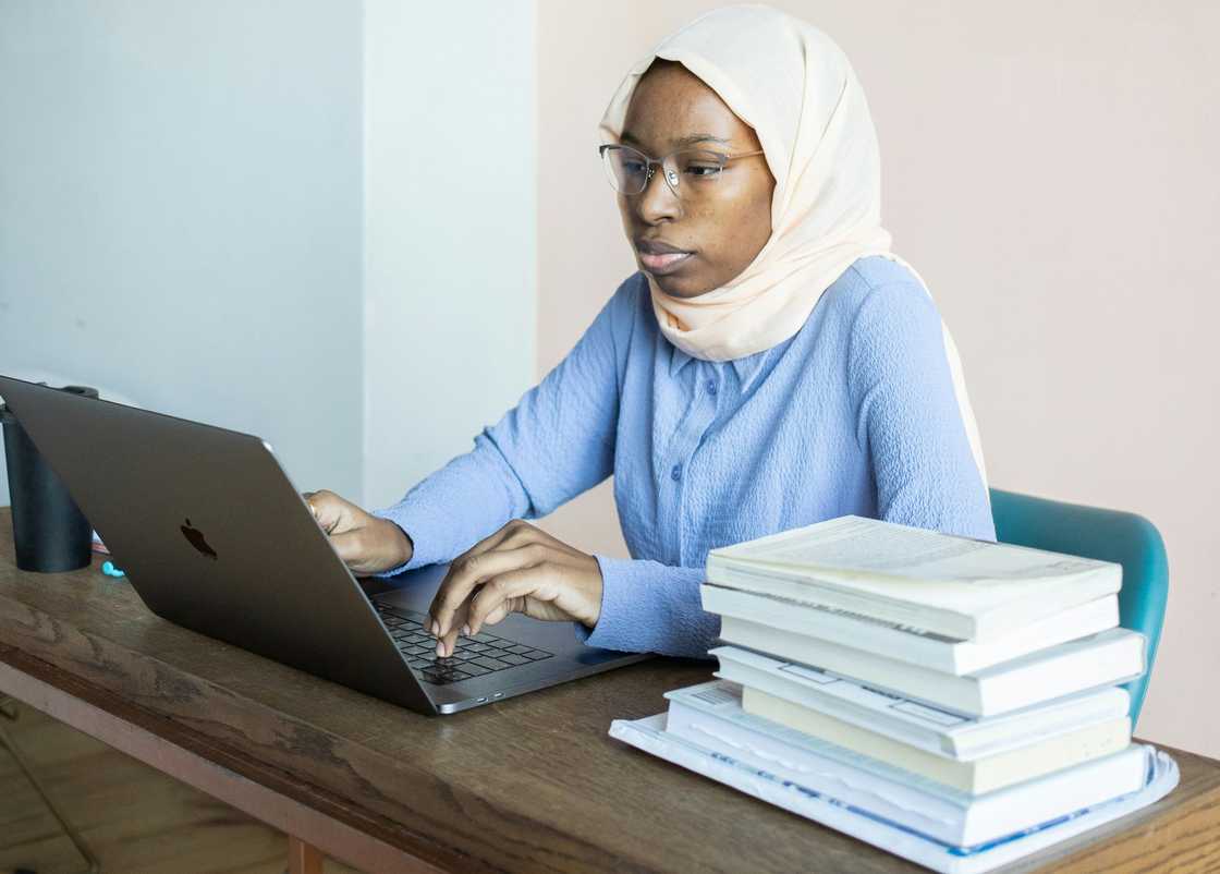 A student using a laptop at a table with books A student using a laptop at a table with books