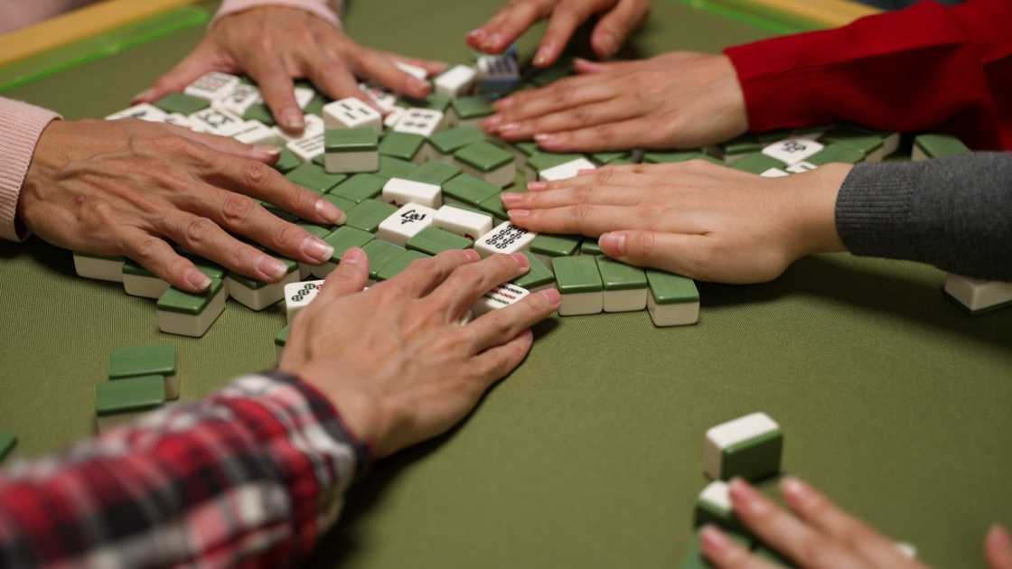 A closeup view of hands mixing tiles on the table with green cloth during a mahjong game. A closeup view of hands mixing tiles on the table with green cloth during a mahjong game.