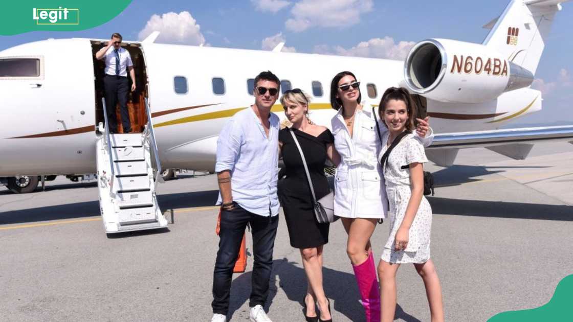 Two women and two men stand on a tarmac in front of a small jet, one woman in pink boots. Two women and two men stand on a tarmac in front of a small jet, one woman in pink boots.