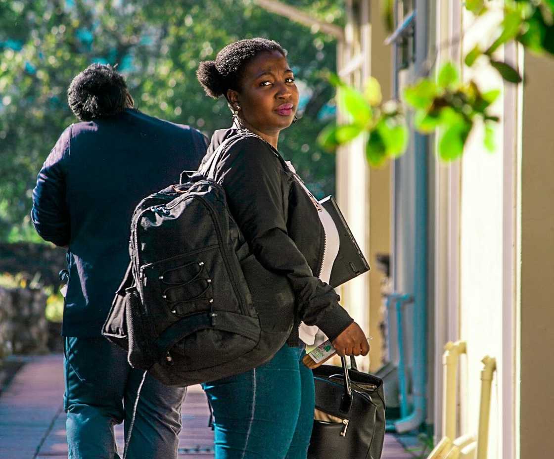A woman walks away with a bag outdoors. A woman walks away with a bag outdoors.