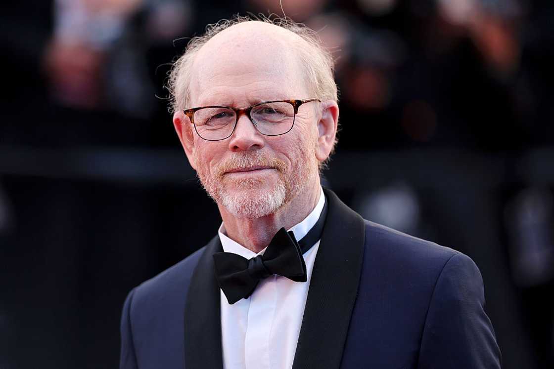 Ron Howard wearing glasses and a black tuxedo with a bow tie, smiling slightly on the red carpet.