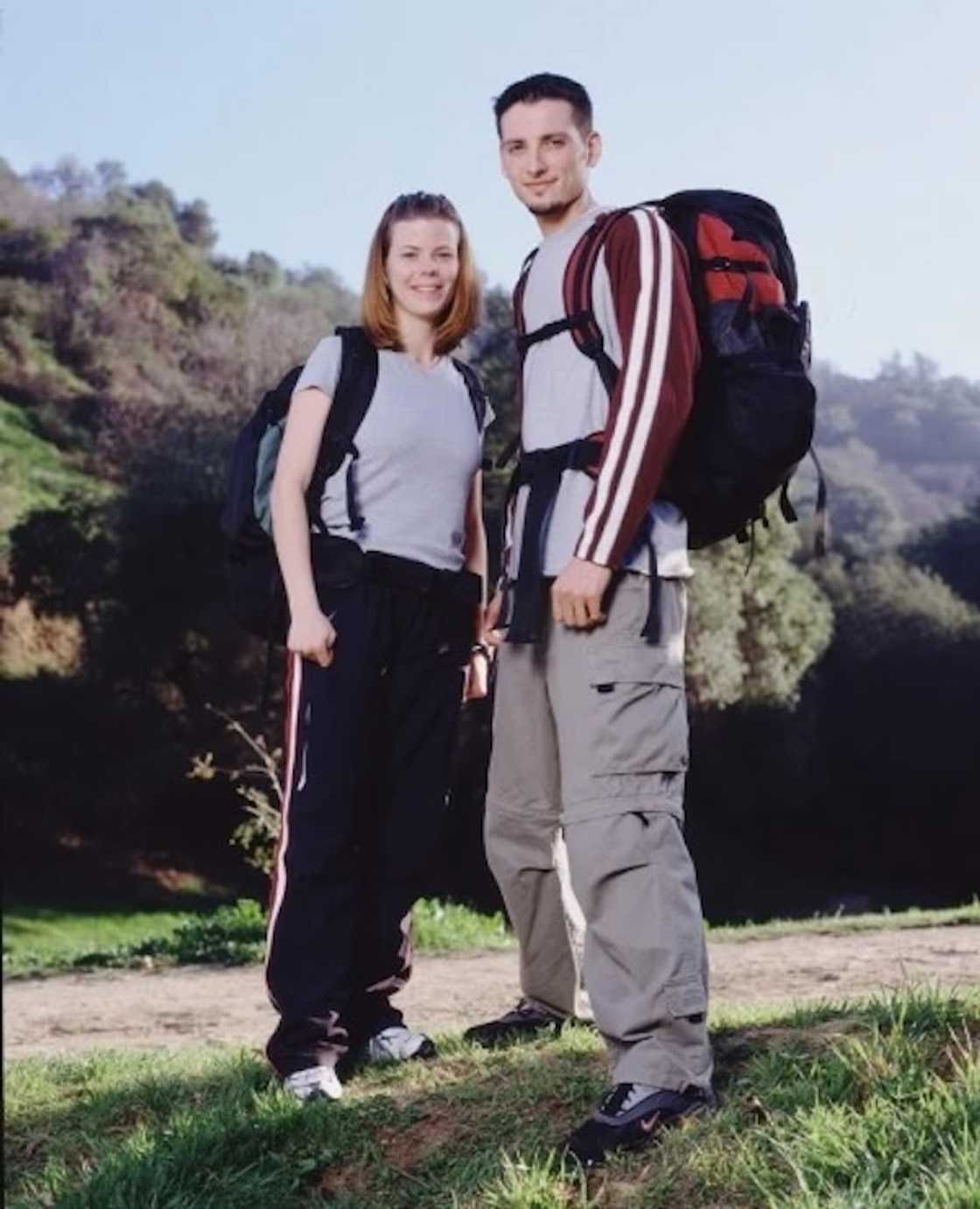 Amanda in a grey top and a man in a maroon striped jacket stand together on a grassy hillside.