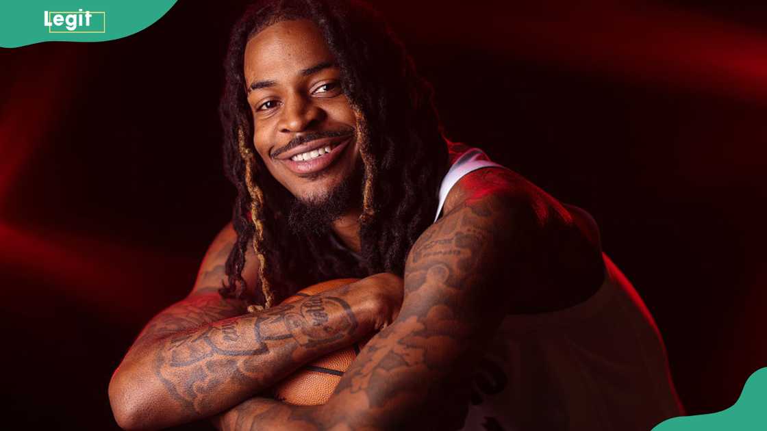 Ja Morant smiling at the camera with his arms folded over a basketball against a red backdrop at Trail Blazers media day, 2026 Ja Morant smiling at the camera with his arms folded over a basketball against a red backdrop at Trail Blazers media day, 2026