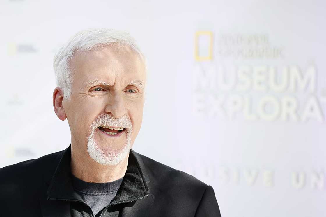 James Cameron with white hair and a mustache, laughing while wearing a black jacket at a National Geographic Museum event. James Cameron with white hair and a mustache, laughing while wearing a black jacket at a National Geographic Museum event.