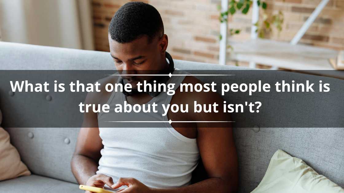 A man in a white vest is sitting on a grey sofa as he texts on a yellow phone A man in a white vest is sitting on a grey sofa as he texts on a yellow phone