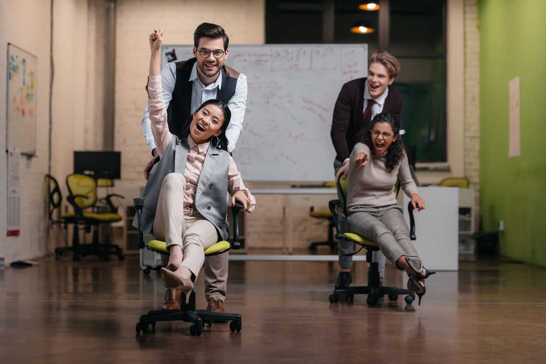 Two men pushing the ladies on swivel chairs in the office.