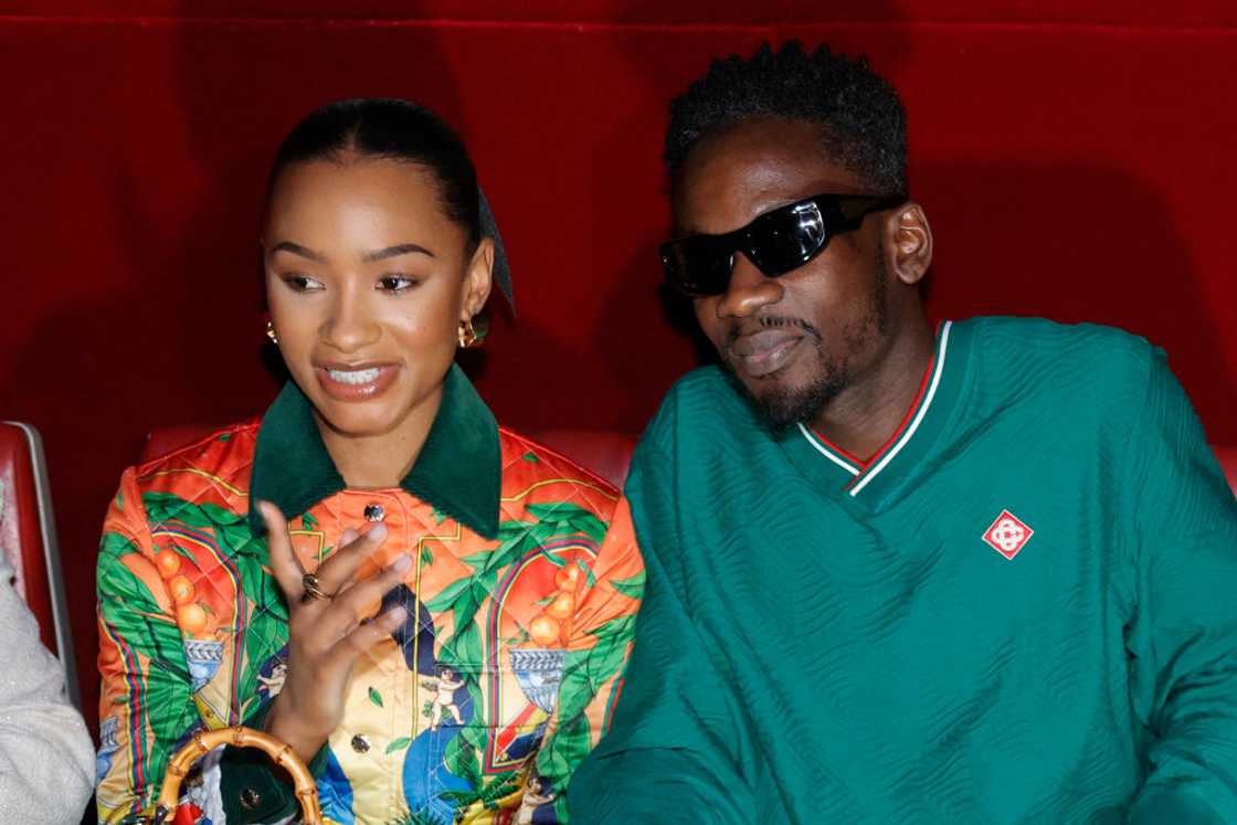 Temi Otedola in a colourful printed outfit beside Mr Eazi in a green tracksuit and sunglasses, seated together at the Casablanca show in Paris