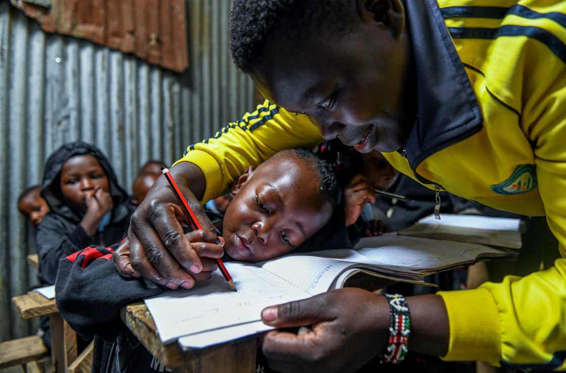 A teacher shows a student how to write letters in a makeshift school A teacher shows a student how to write letters in a makeshift school