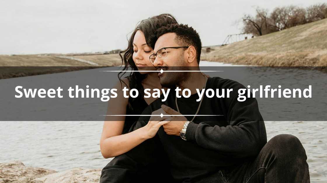 A man and a woman in black outfits are holding hands while sitting beside a water body