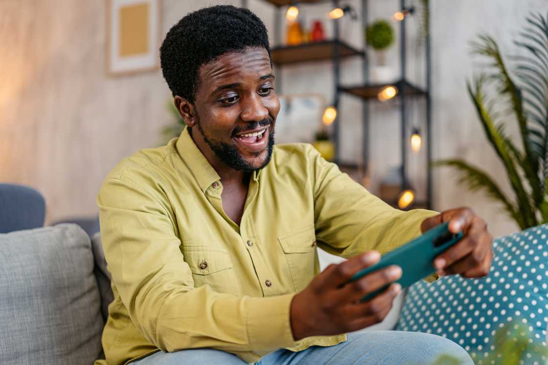 A man sitting on the sofa and playing video games on the phone.