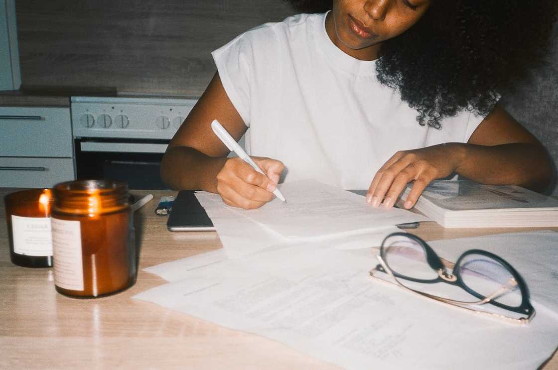 A woman writing in a notebook at a table with papers, glasses, and lit candles nearby. A woman writing in a notebook at a table with papers, glasses, and lit candles nearby.