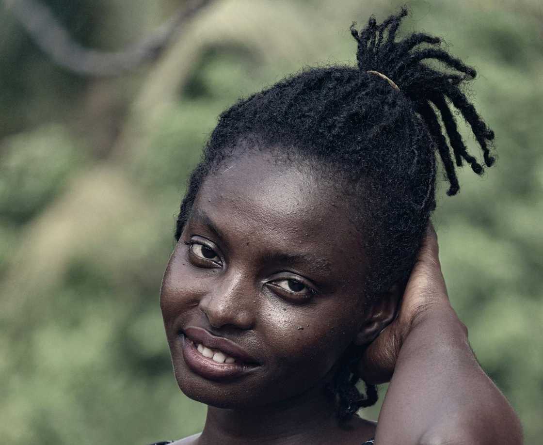 A smiling woman outdoors with her hair tied back, touching her head. A smiling woman outdoors with her hair tied back, touching her head.