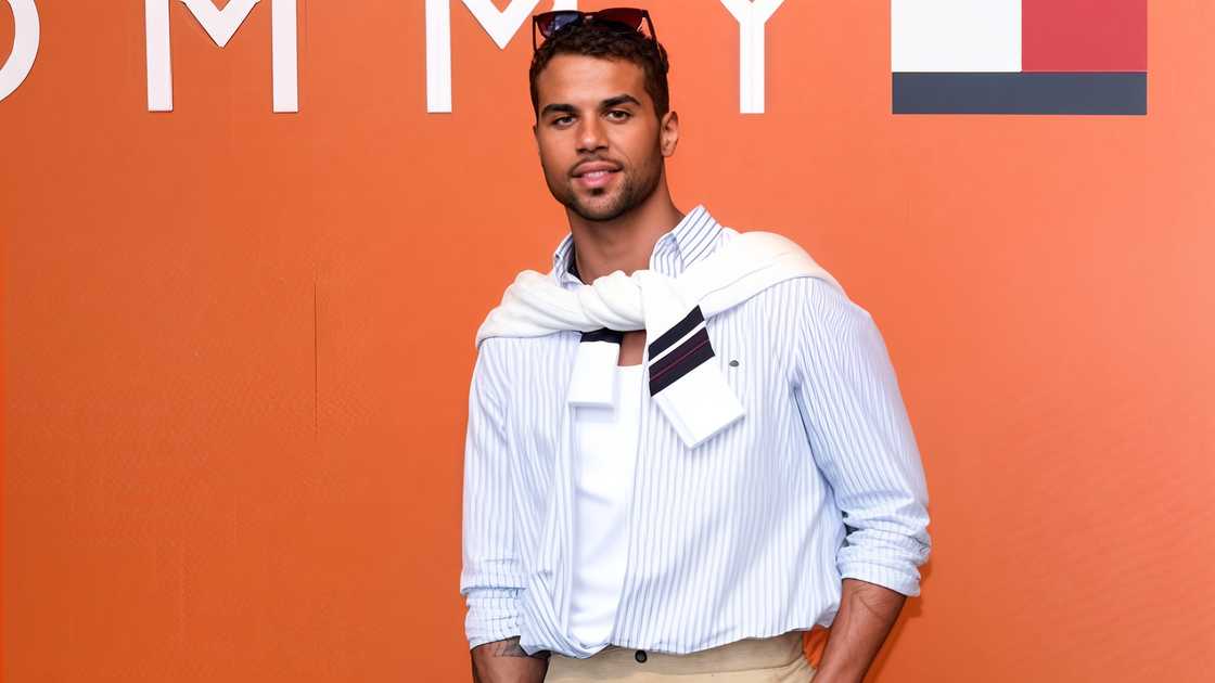 Mason Gooding poses in front of a Tommy Hilfiger sign.