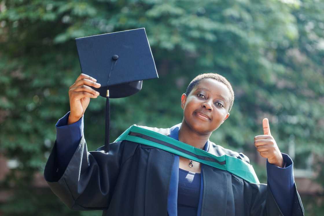 A lady in dark standing in public park holding diploma high. A lady in dark standing in public park holding diploma high.