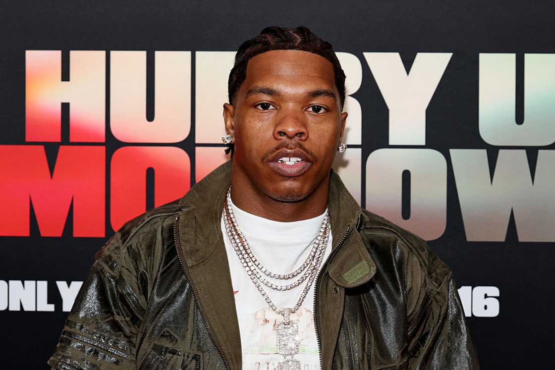 Lil Baby wearing a dark green jacket, white t-shirt and chains at a red carpet.