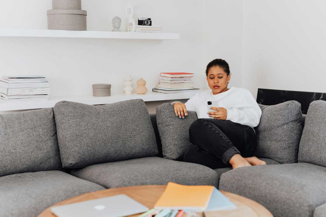 A woman scrolls through a phone while seated on a sofa