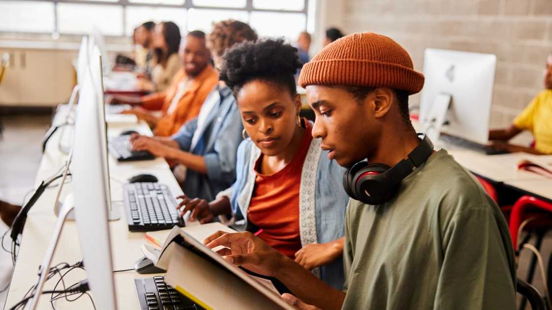 Male and female students read books in front of computers in a library. Male and female students read books in front of computers in a library.