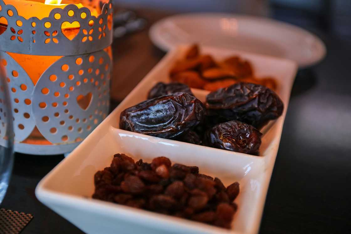 A close-up of raisins and dates on a white rectangular dish with compartments