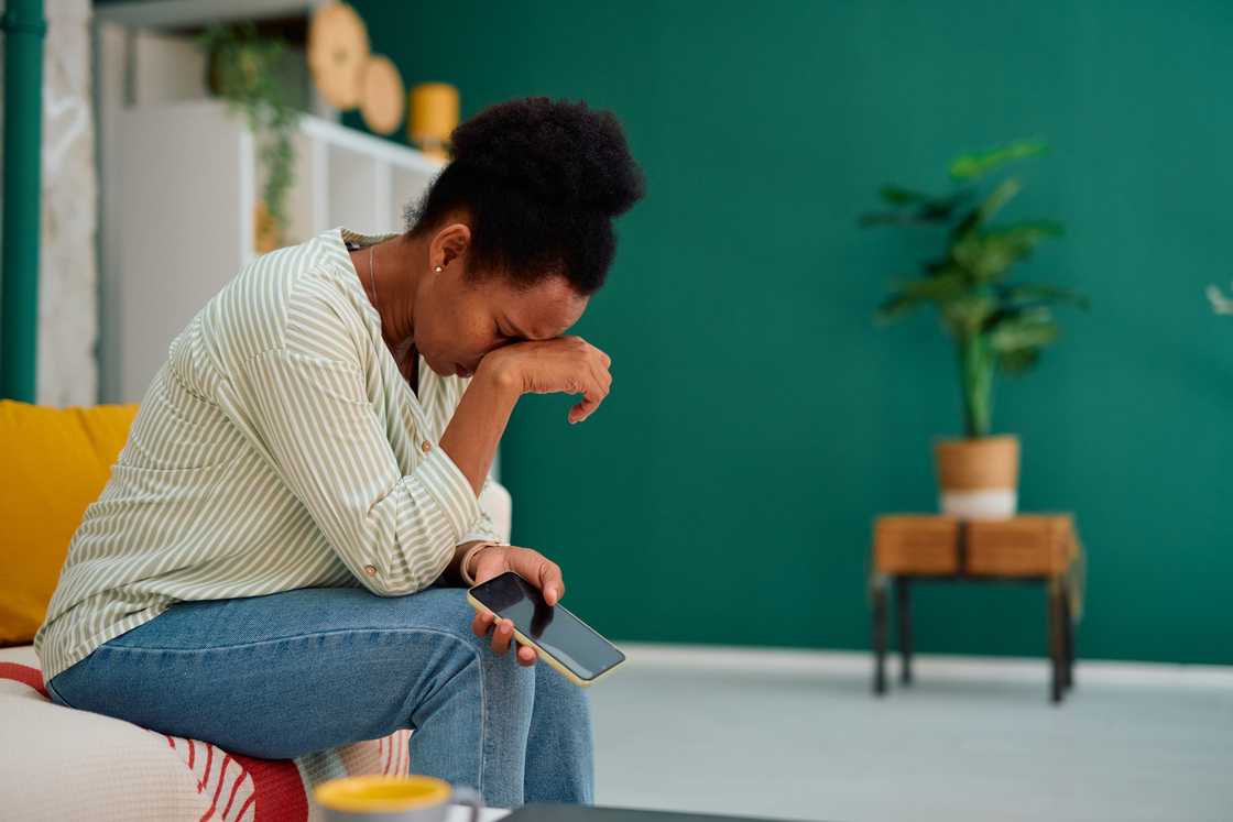 A sad woman crying while holding mobile phone at home