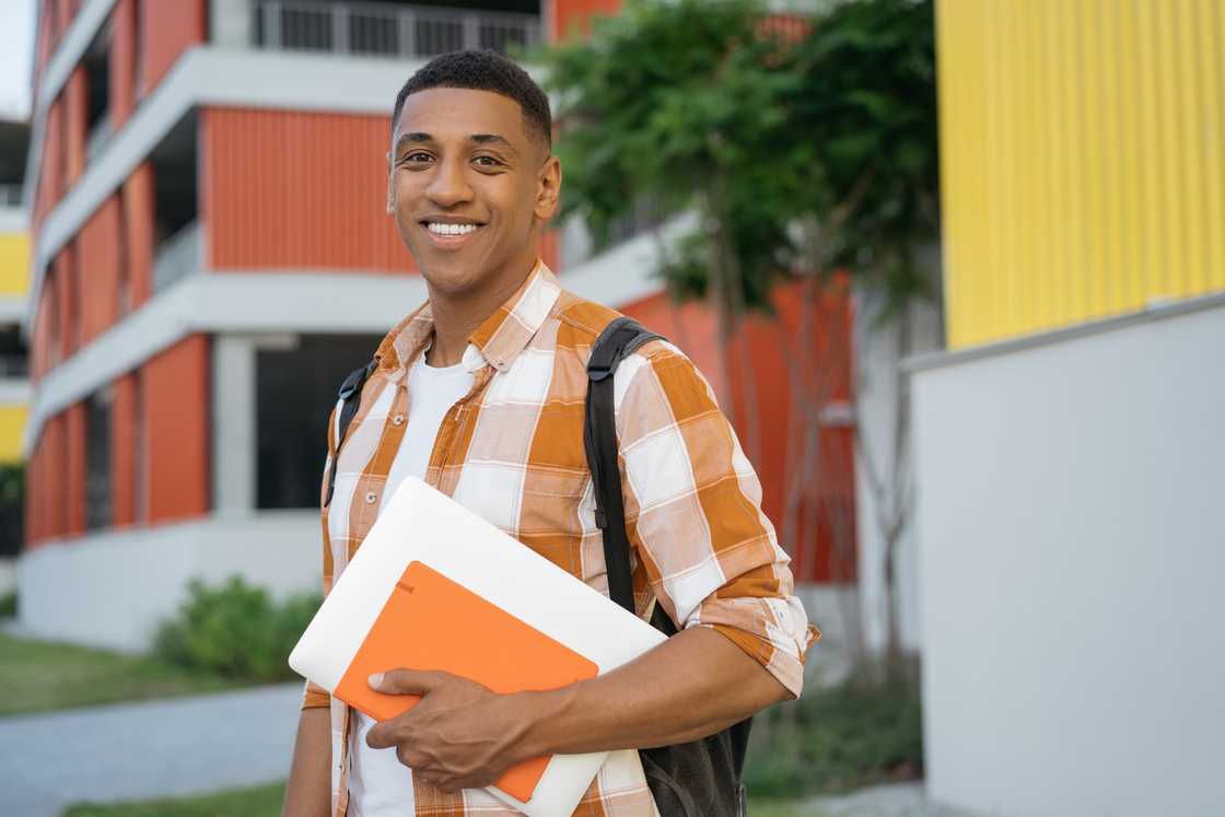 A male student walking in university campus holding books. A male student walking in university campus holding books.