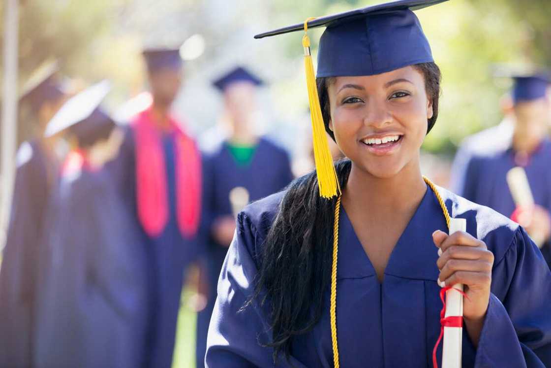 A lady dressed in a graduation gown and cap posing for a photo after the graduation ceremony A lady dressed in a graduation gown and cap posing for a photo after the graduation ceremony